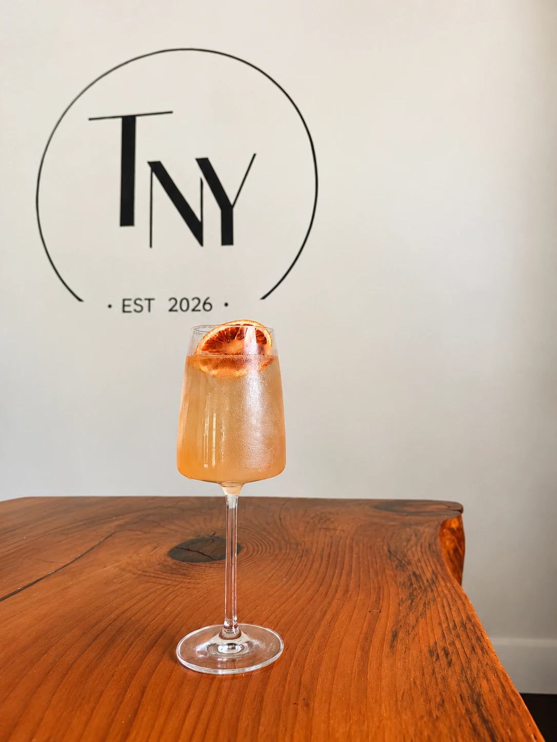 House cocktail with a dried orange wheel in front of the TNY logo wall