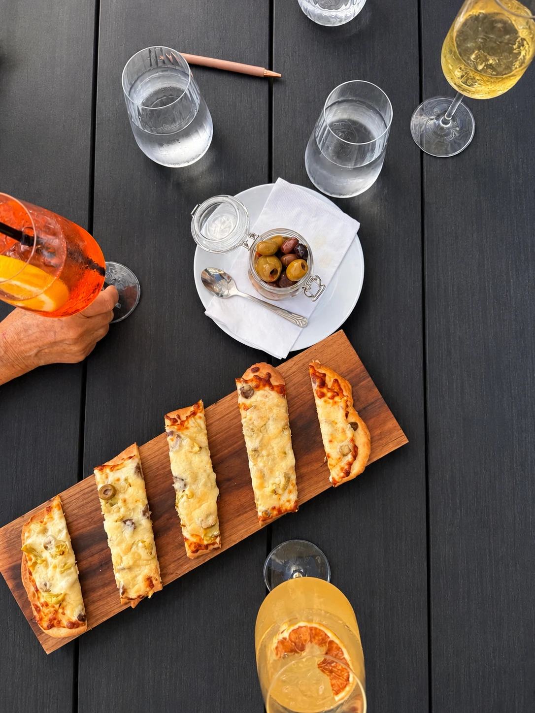 Flatbread board, marinated olives and cocktails on the patio table